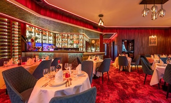 A restaurant with round tables, chairs, and a bar area with shelves of bottles.
