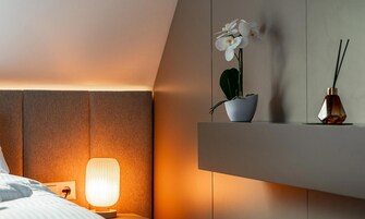 Habitación de hotel con una cama, una lámpara de noche, una orquídea en maceta y una botella decorativa en un estante.