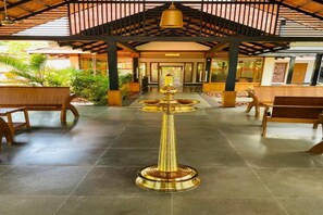 A lobby with a central golden lamp, wooden benches, and a tiled floor. - Niraamaya Retreats Vaidekam Kannur (Talipparamba)