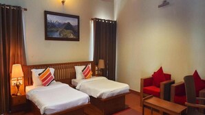 Habitación de hotel con dos camas, un sofá rojo, una mesa de madera y un cuadro en la pared.