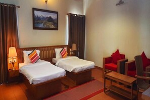 A hotel room with two beds, a red sofa, a wooden table, and a painting on the wall. - Niraamaya Retreats Vaidekam Kannur (Talipparamba)