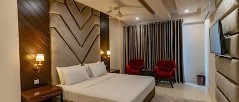 A hotel room with a bed, a nightstand, a TV, a ceiling fan, and a window with curtains.