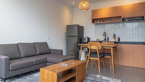 A modern living room with a sofa, a wooden coffee table, and a kitchen area with wooden cabinets and a microwave. - Cypress Villa by Zuzu (Ungasan)