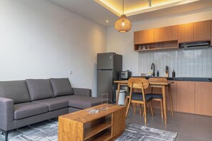 Een moderne woonkamer met een bank, een houten salontafel en een keukenhoek met houten kasten en een magnetron.