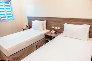 Habitación de hotel con dos camas, cabecero de madera, mesitas de noche con lámparas, un teléfono y una ventana con persianas.