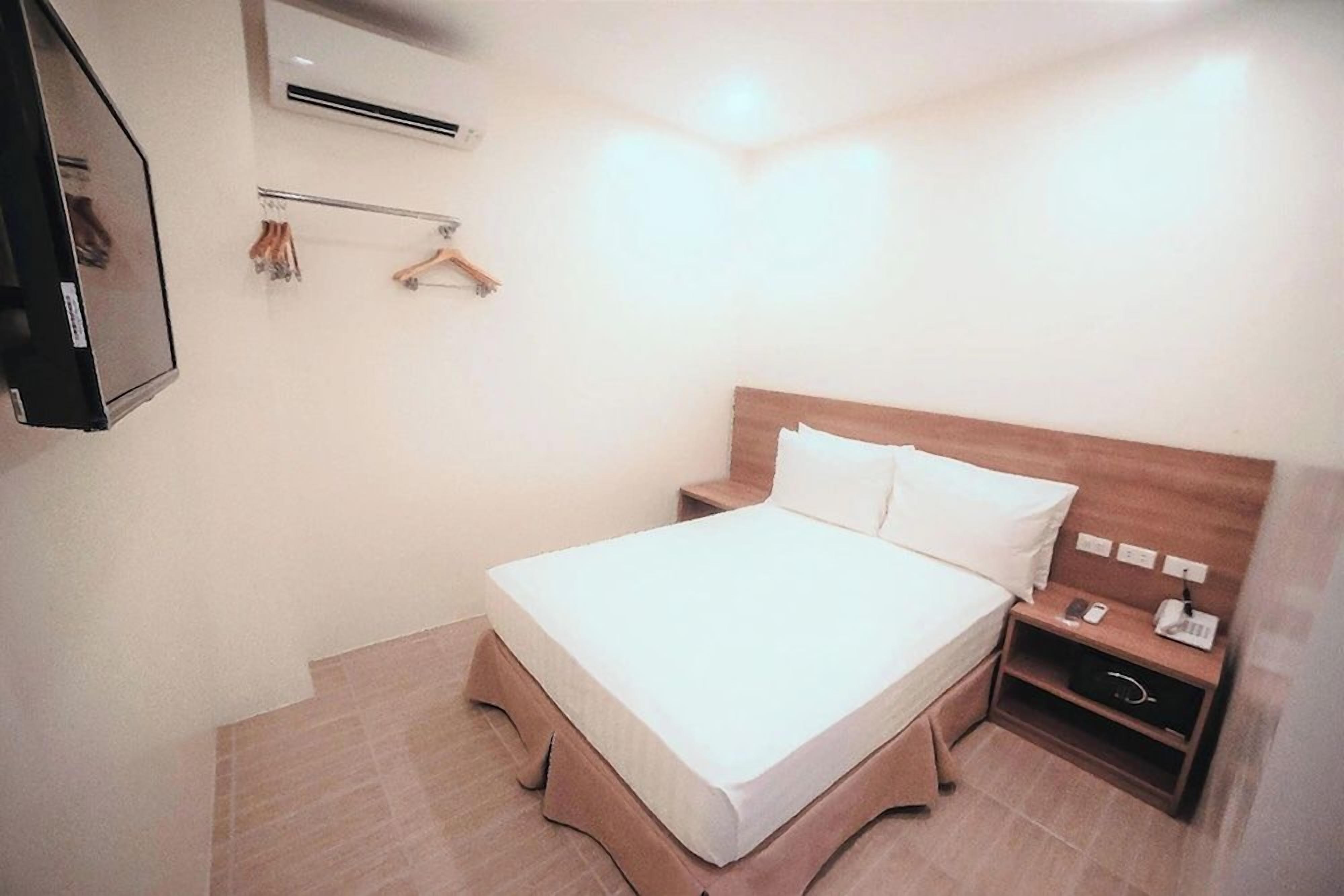 A hotel room with a bed, bedside table, and a mirror.