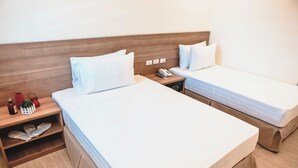 Hotellihuone, jossa on kaksi sänkyä, puinen pääty, yöpöytä, jossa on puhelin, ja kenkäteline.