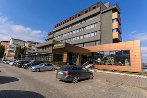 Un hotel de diseño moderno, con una entrada destacada de fachada de vidrio y un estacionamiento con varios autos.