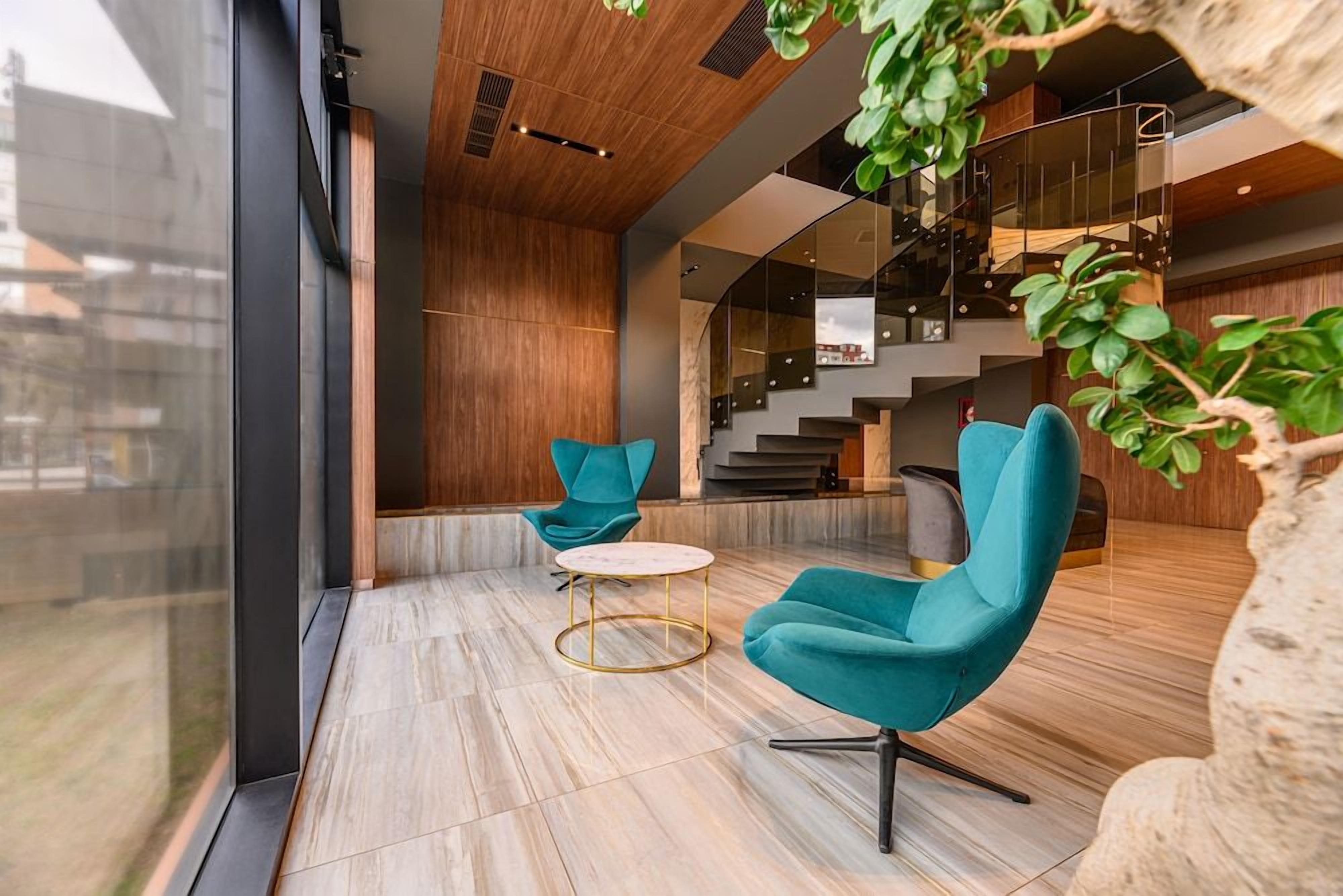 A modern interior with a seating area featuring teal chairs and a marble-tiled floor.