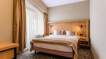 A hotel room with a bed, bedside tables, a desk, and a patterned floor.