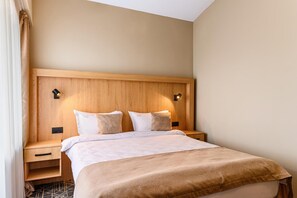 Habitación de hotel con cabecera de madera, dos mesitas de noche, cama con ropa blanca y dos lámparas fijadas a la pared.