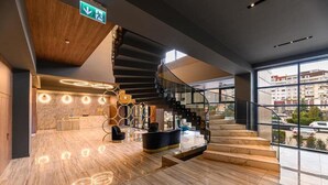 En moderne hotellobby med et marmorgulv, en reception, en trappe og store vinduer med udsigt over byen.