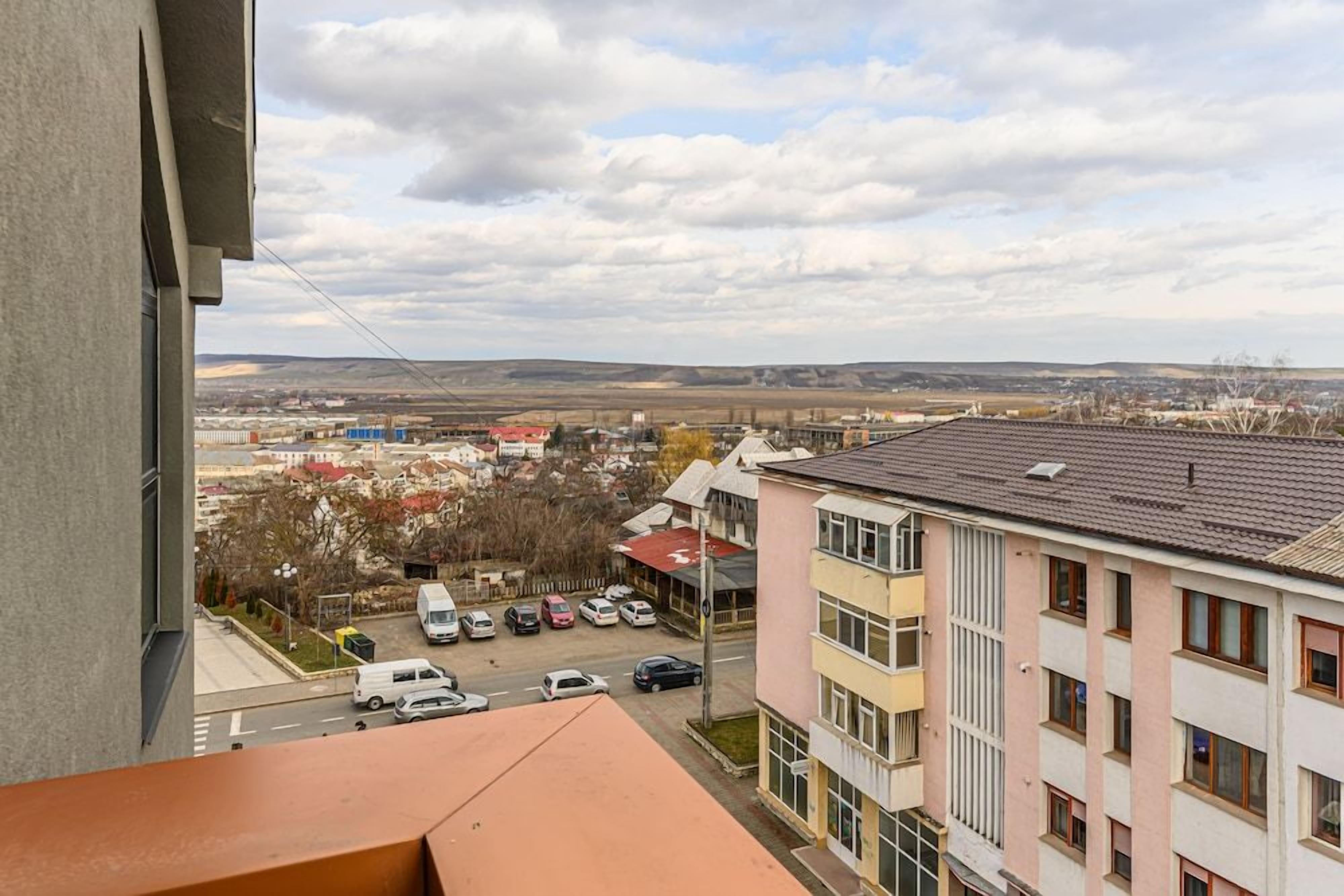 A residential area with multi-story buildings, a parking lot, and a distant view of a town.
