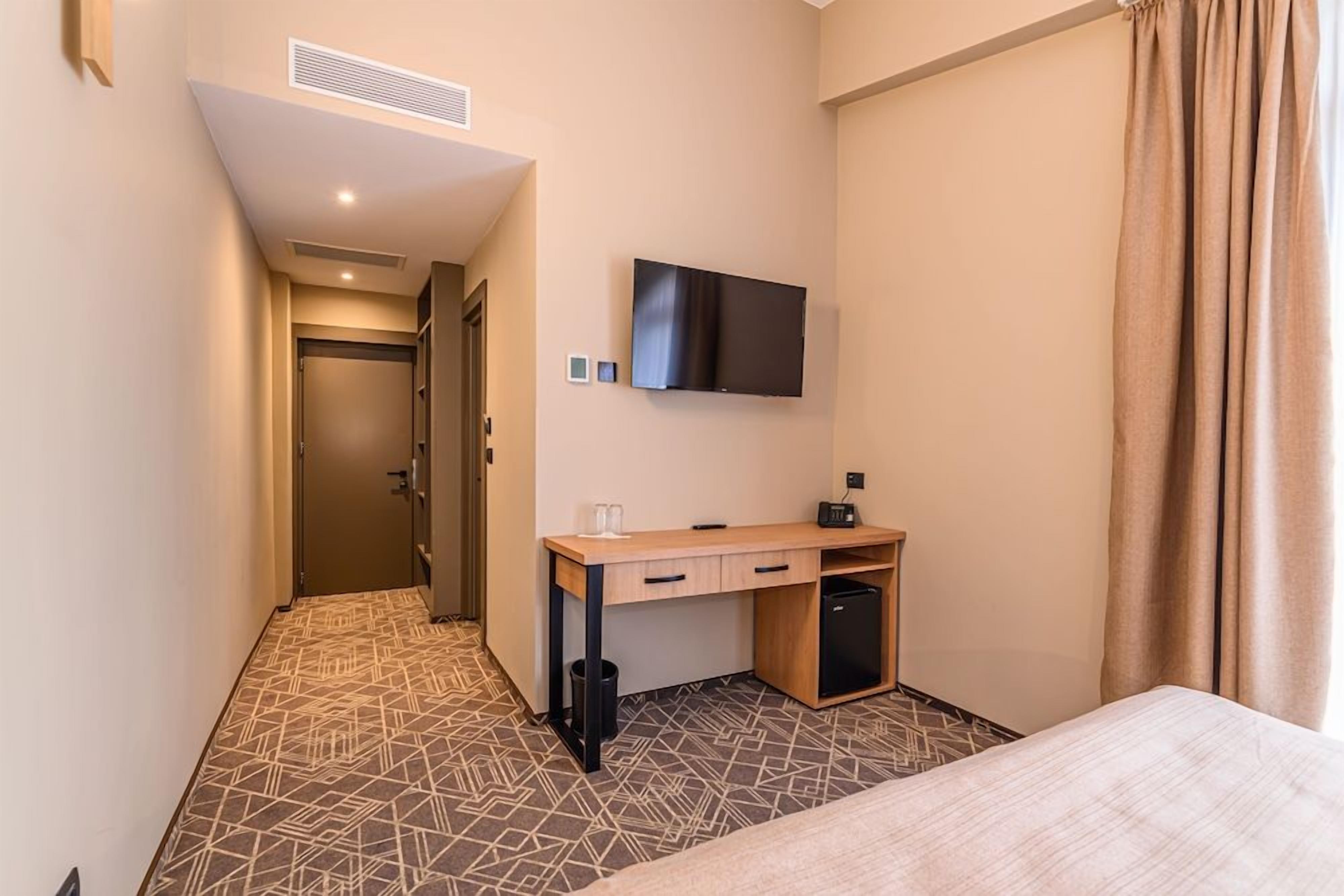 A hotel room with a bed, a desk with a computer, a television, and a patterned floor.