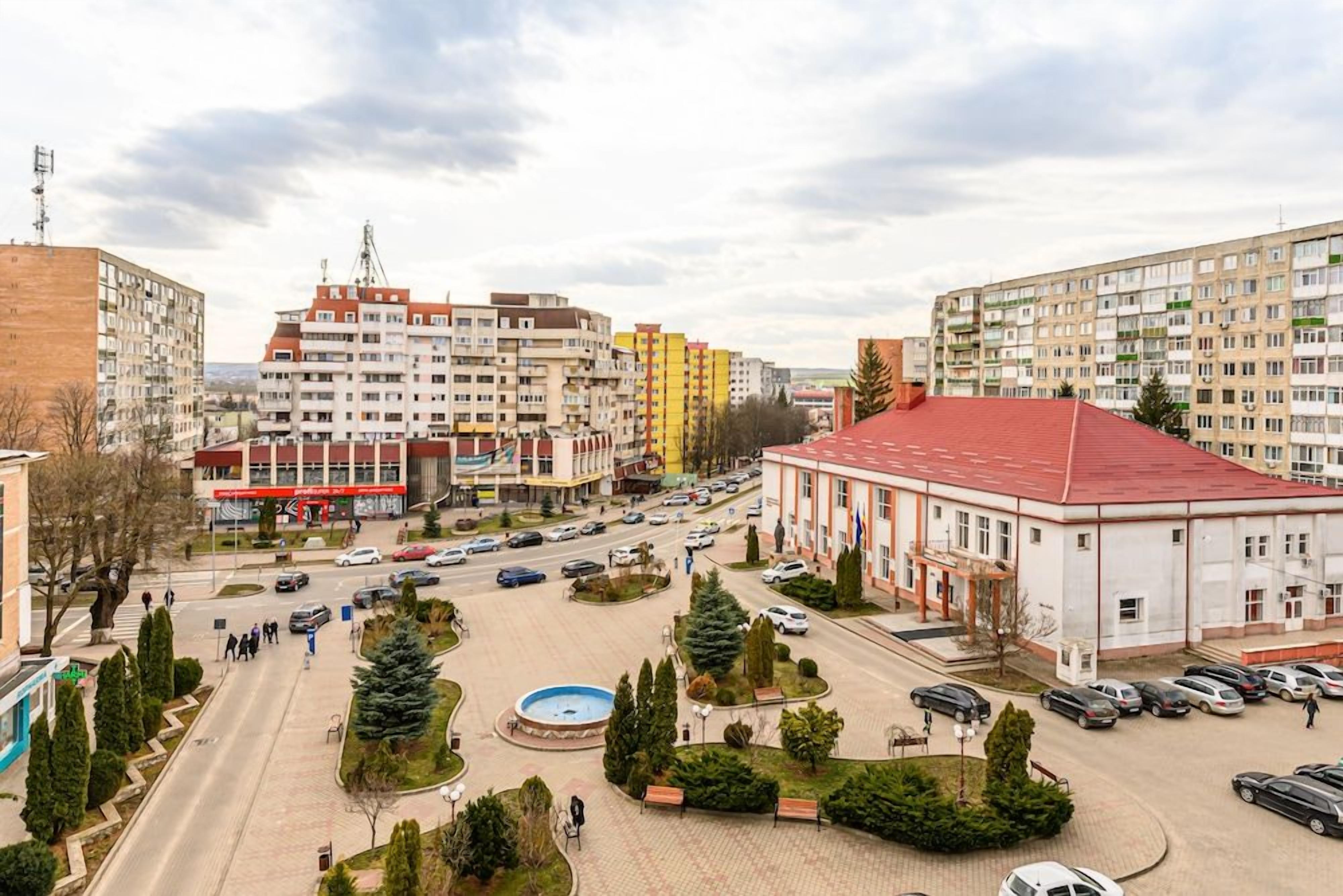 A city square with buildings, a fountain, and parked cars.