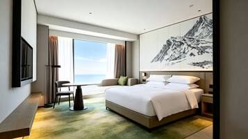 A hotel room with a bed, a desk, a chair, a large window with curtains, and a wall-mounted TV.