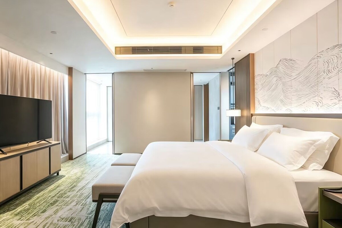 A hotel room with a large bed, a flat-screen TV, a desk, and a wall-mounted artwork.
