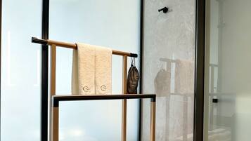 A modern bathroom with a glass shower enclosure, a wooden towel rack, and a marble-tiled floor.