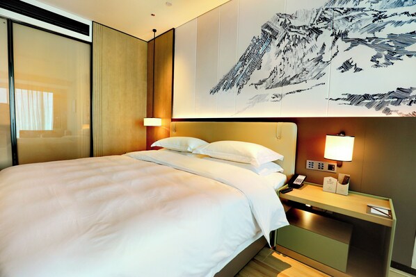 A hotel room with a bed, a nightstand, a telephone, and a wall-mounted control panel.