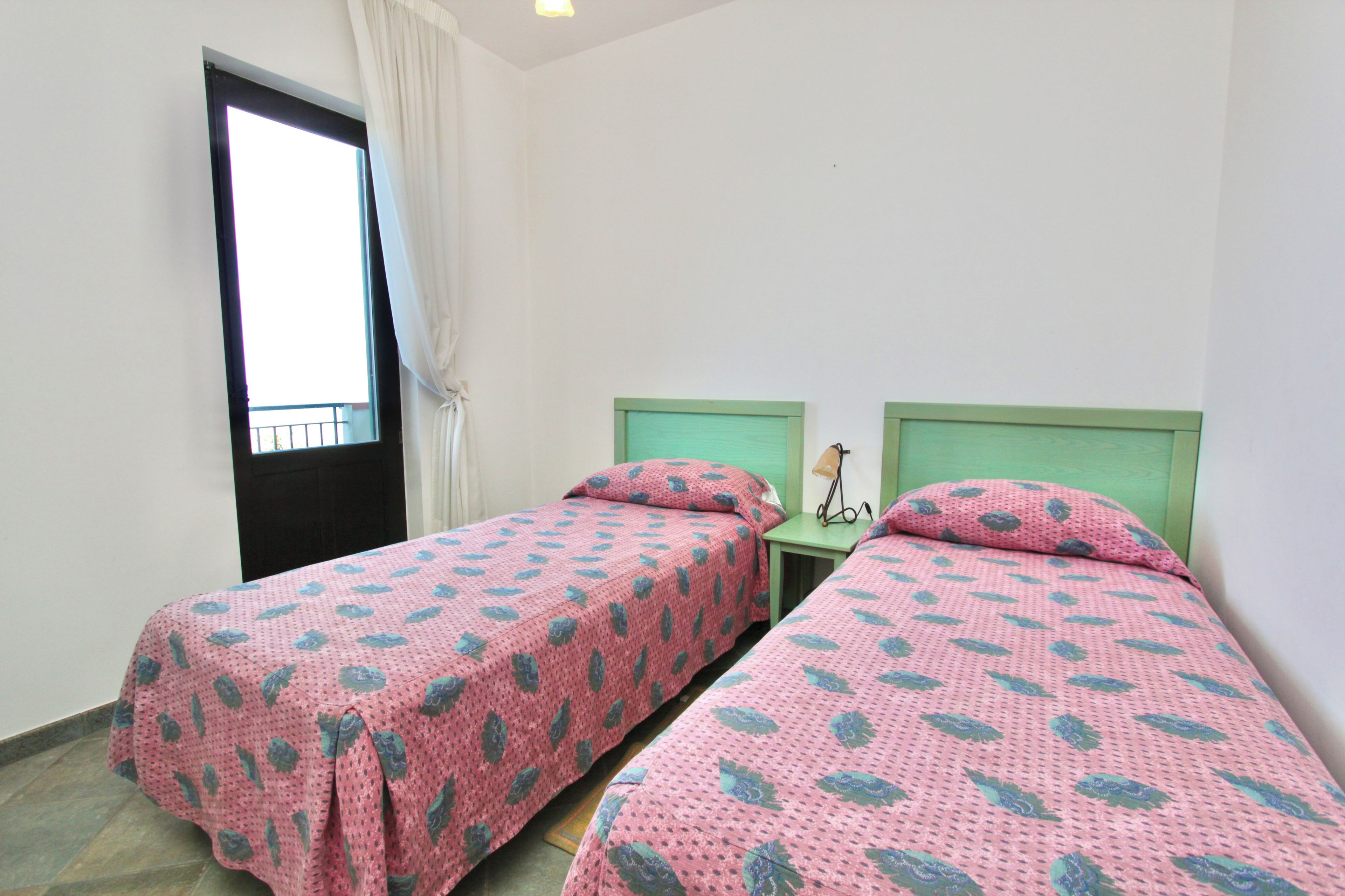 Una habitación con dos camas individuales, una mesita con lámpara y una ventana con cortinas.