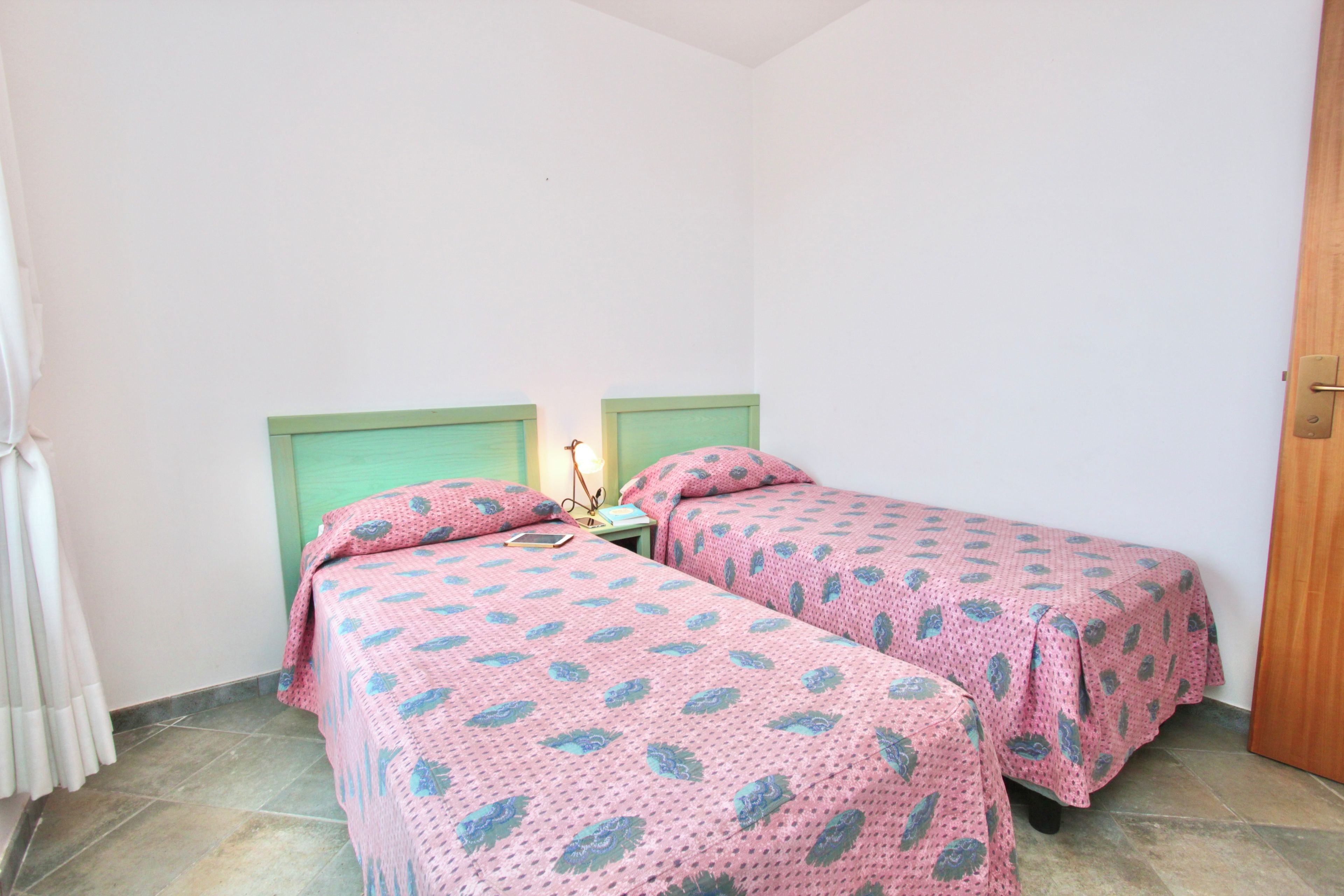 Ein kleines Zimmer mit zwei Einzelbetten, passenden Kopfteilen und Fußteilen, einem Nachttisch mit Lampe und einer Tür.