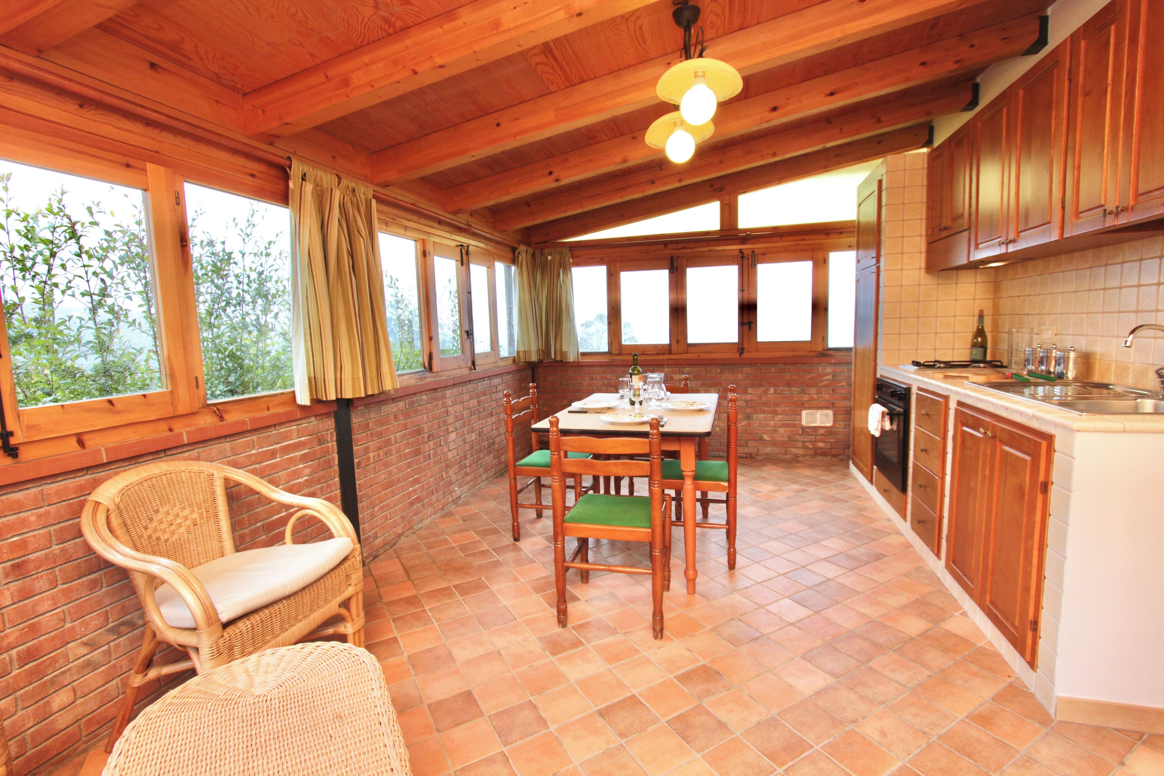 A wooden interior with a dining table, chairs, a kitchen area, and large windows.