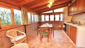 A wooden interior with a dining table, chairs, a kitchen area, and large windows.