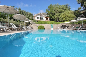A swimming pool with lounge chairs and umbrellas, surrounded by greenery and a building in the background. - Residence with swimming pool in Capo d'Orlando (Capo d'Orlando)