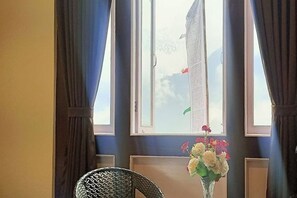 Una habitació amb finestra, cortines, una cadira i un vas amb flors.