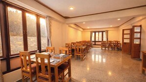 A conference room with multiple tables and chairs, large windows, and a door. - Ecotel Lachung (Chungthang)