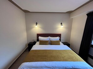 Habitació d'hotel amb un llit gran, dues taules de nit i làmpades penjades a la paret.