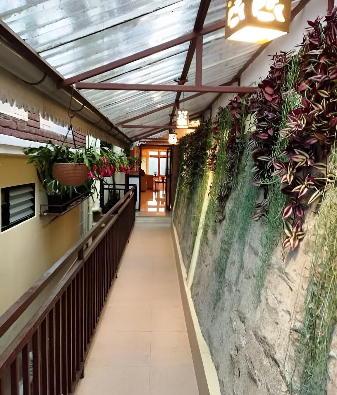A corridor with a metal roof, potted plants, and a view into a room with a door.