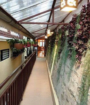 A corridor with a metal roof, potted plants, and a view into a room with a door. - Yashshree Karbari Resorts & SPA (Namchi)