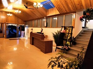 A reception area with a wooden reception desk, a staircase, and potted plants. - Yashshree Karbari Resorts & SPA (Namchi)