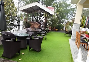 Un espace extérieur aménagé en terrasse, avec des tables et des chaises, entouré de verdure et délimité par une clôture blanche.