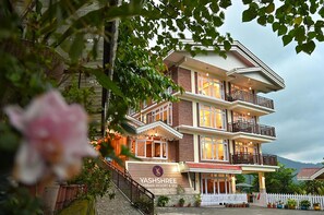 Un immeuble à plusieurs étages doté de balcons, d’un escalier et d’une enseigne indiquant le nom de l’établissement : Yashshree Arbari Resort & Spa.