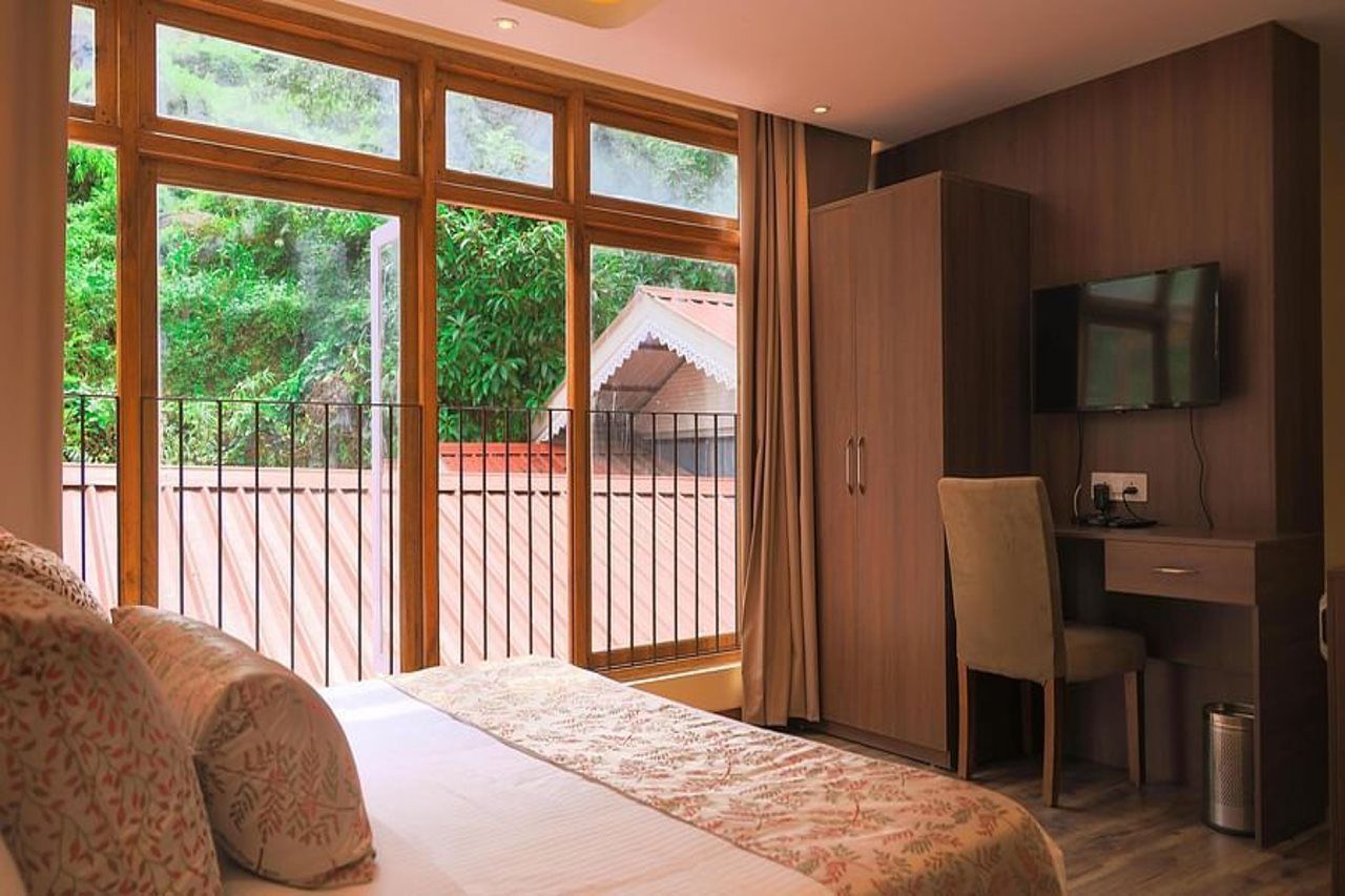Ein Schlafzimmer mit Bett, Schreibtisch, Stuhl, Fernseher und einem Balkon mit Blick ins Grüne.