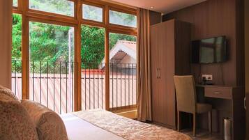 Ein Schlafzimmer mit Bett, Schreibtisch, Stuhl, Fernseher und einem Balkon mit Blick ins Grüne.