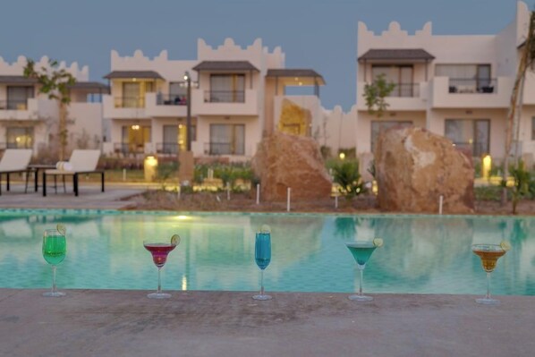 A pool area with multiple lounge chairs and a row of colorful cocktails. - The Fern Sattva Resort, Little Rann of Kutch (Dasada)