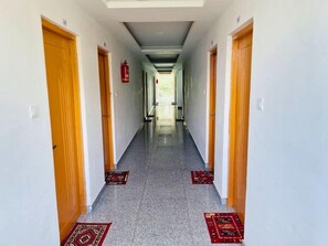 Un couloir bordé de portes de part et d’autre, un extincteur accroché au mur et des tapis à motifs sur le sol.