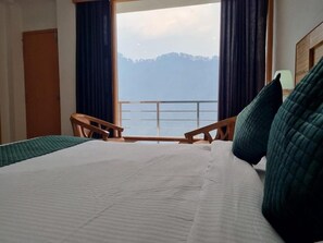 Una camera d'albergo con un letto grande, vista su un balcone e una sedia di legno.