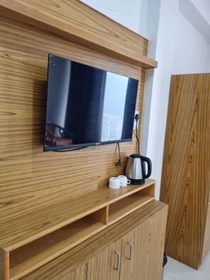 Un'unità di intrattenimento in legno con una televisione a schermo piatto, un bollitore e due tazze.