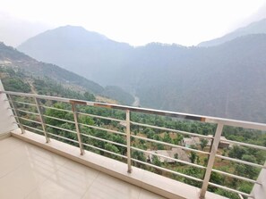 Un balcon doté d’une rambarde en métal, donnant sur une vallée verdoyante et sur des montagnes lointaines.