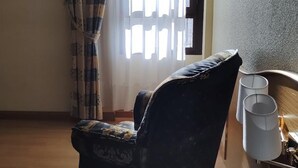 Ein Hotelzimmer mit einem Bett, einem Sessel, einem Nachttisch mit Lampe und einem fenster mit Vorhängen.