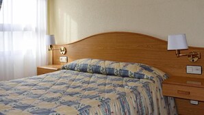 Ein Hotelzimmer mit einem Holzkopfteil, einem Bett mit gesteppter Bettdecke, einem Nachttisch mit Lampe und einer Wandkonsole.