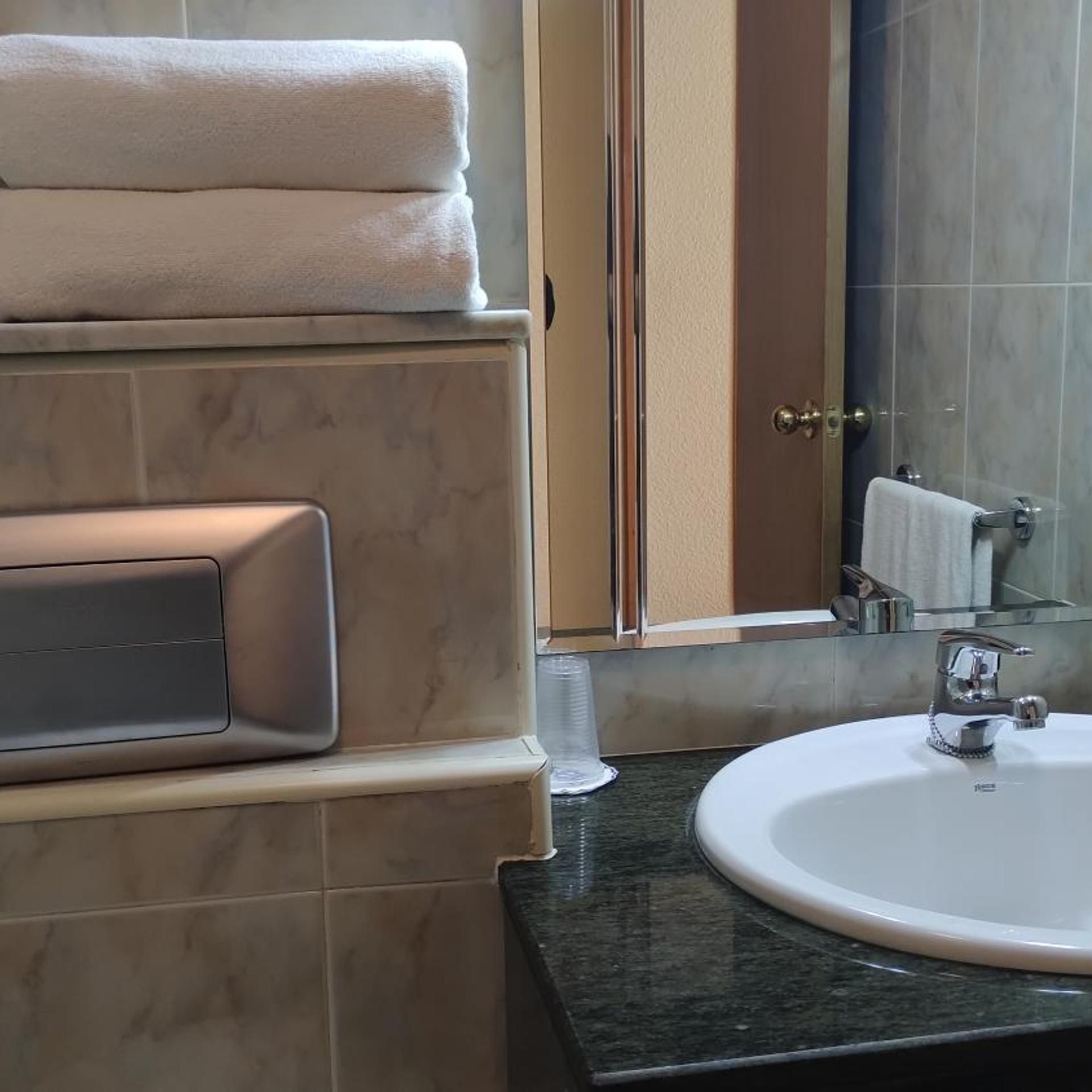 Un baño con pared de azulejos de mármol, un lavamanos con grifo cromado y un perchero con toallas dobladas.