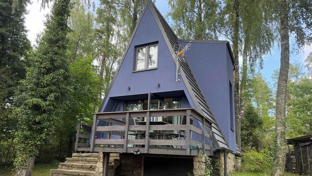 A house with a steeply pitched roof, a balcony with a wooden railing, and a stone staircase leading to the entrance. - Lake Bieszkowice Holiday Cabin (Bieszkowice)