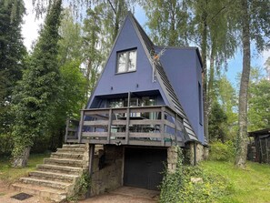 A house with a steeply pitched roof, a balcony with a wooden railing, and a stone staircase leading to the entrance. - Lake Bieszkowice Holiday Cabin (Bieszkowice)