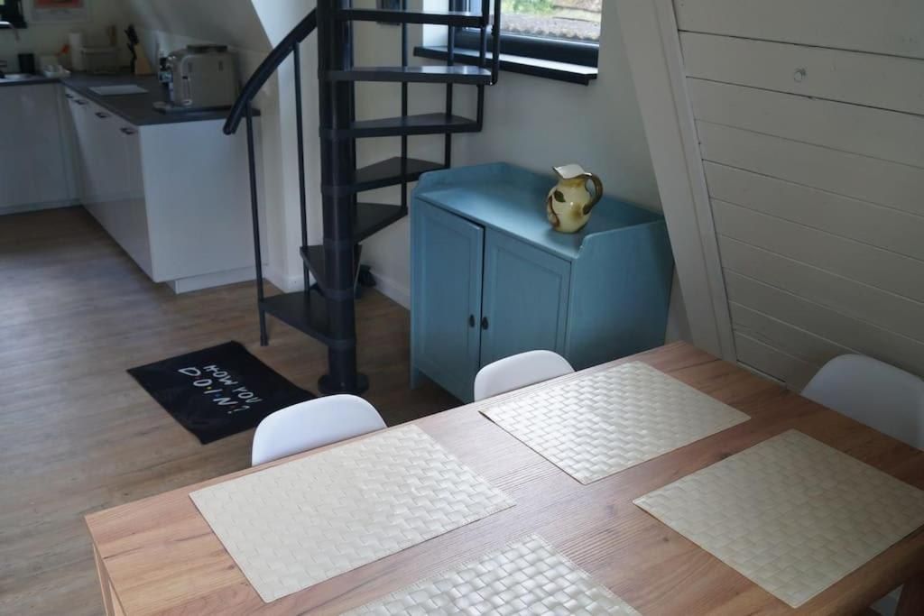 Un coin repas avec une table en bois, des chaises blanches, un buffet bleu et un escalier en colimaçon noir.