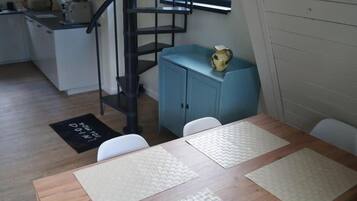 Un coin repas avec une table en bois, des chaises blanches, un buffet bleu et un escalier en colimaçon noir.